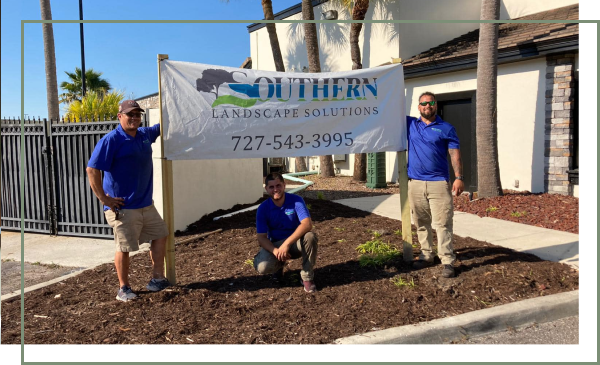A team from Southern Landscape Solutions on a backyard landscape construction jobsite in Clearwater, posing with their company banner.