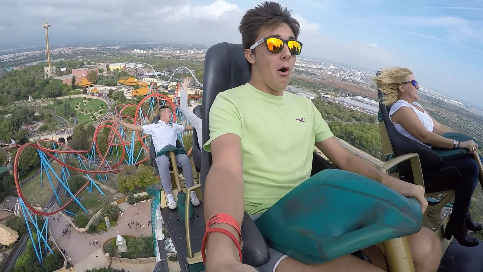 Óscar, con gafas de sol, grabándose con una cámara de acción en lo alto de una atracción, con el parque a sus pies