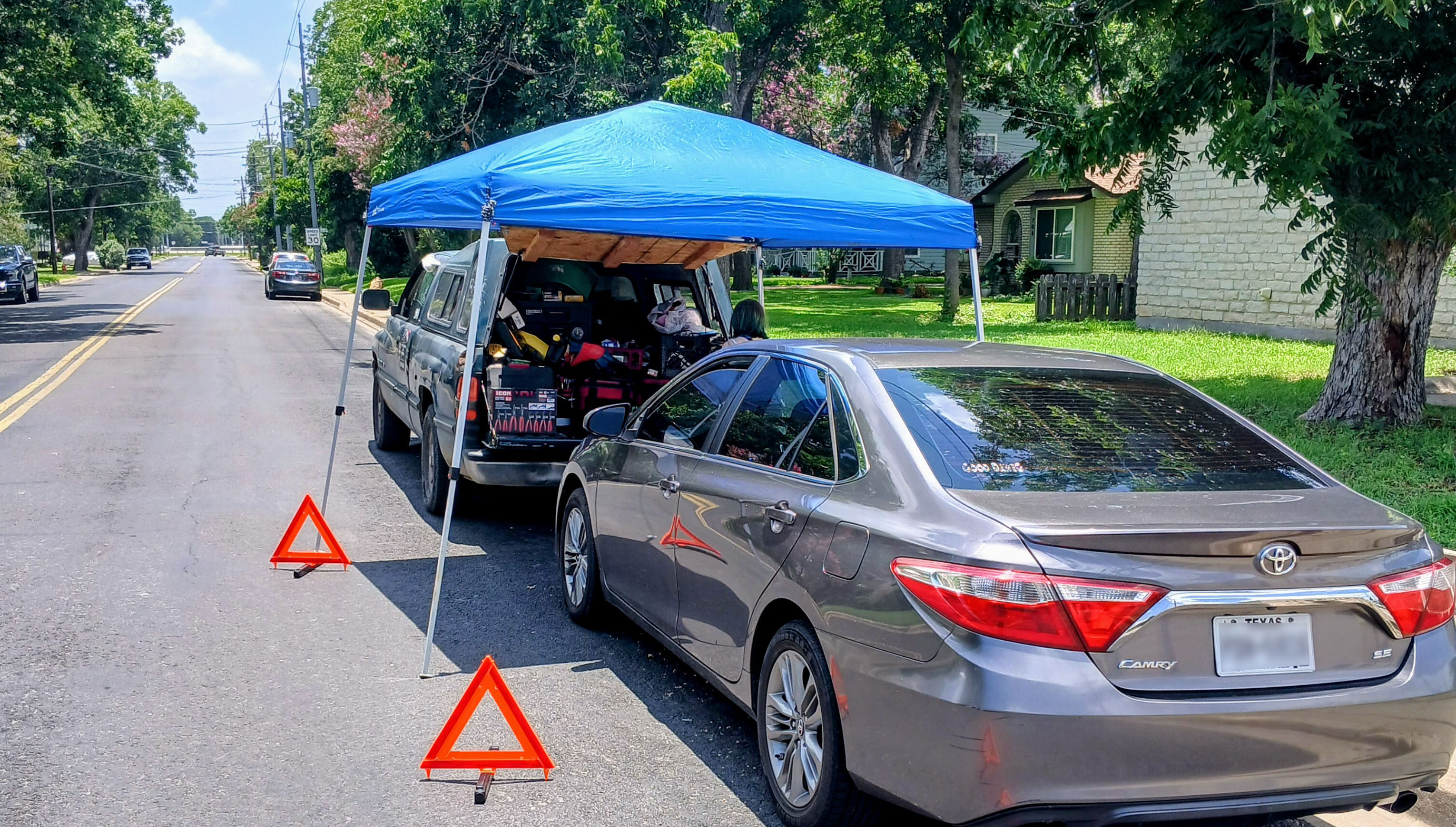 Honest Joe's Auto mobile mechanic service setup on a residential street in Bastrop, TX — service truck, canopy, and warning triangles deployed for roadside repair