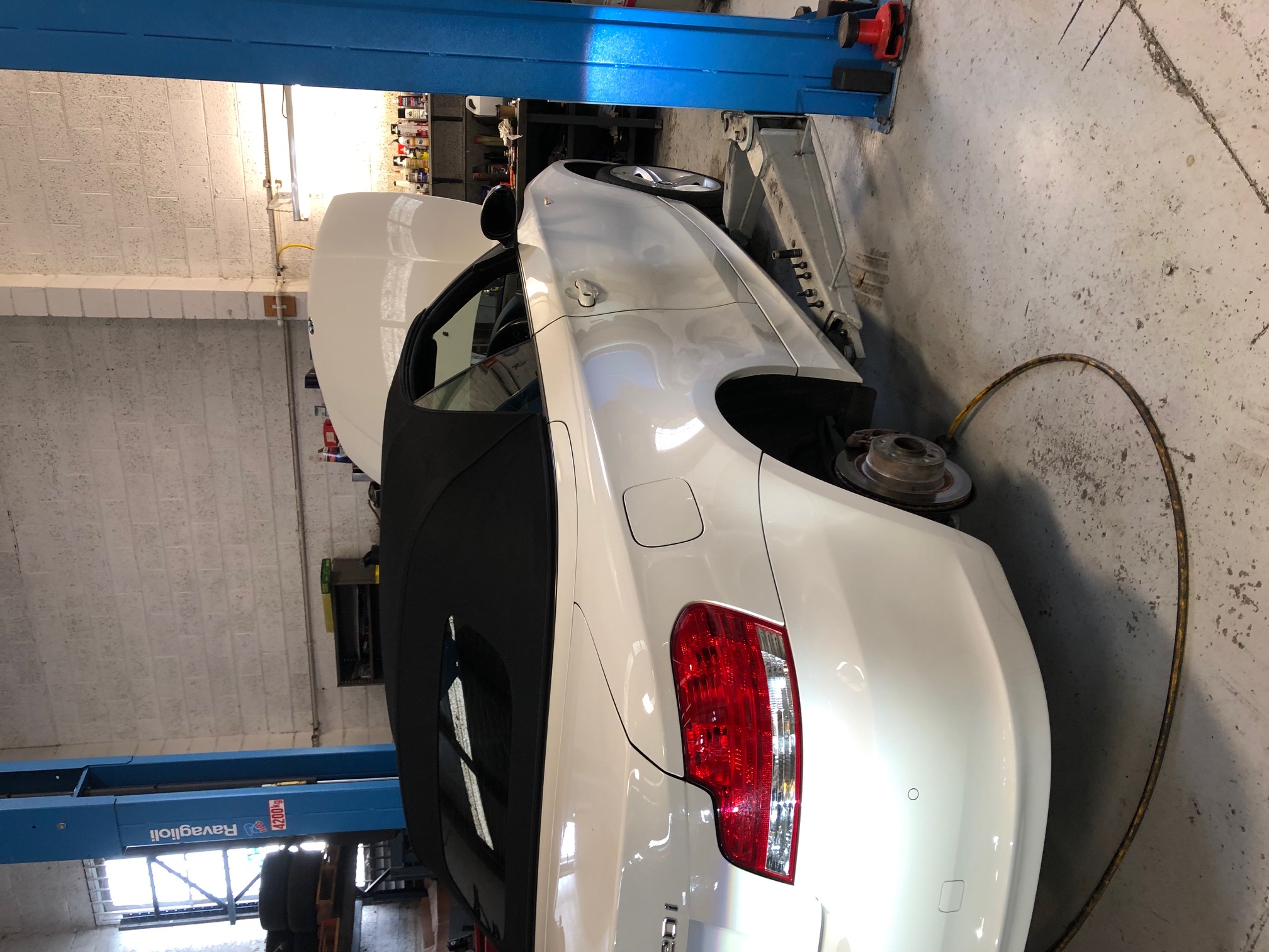 White convertible car raised on a workshop hoist with wheel removed for a brake and tyre inspection.