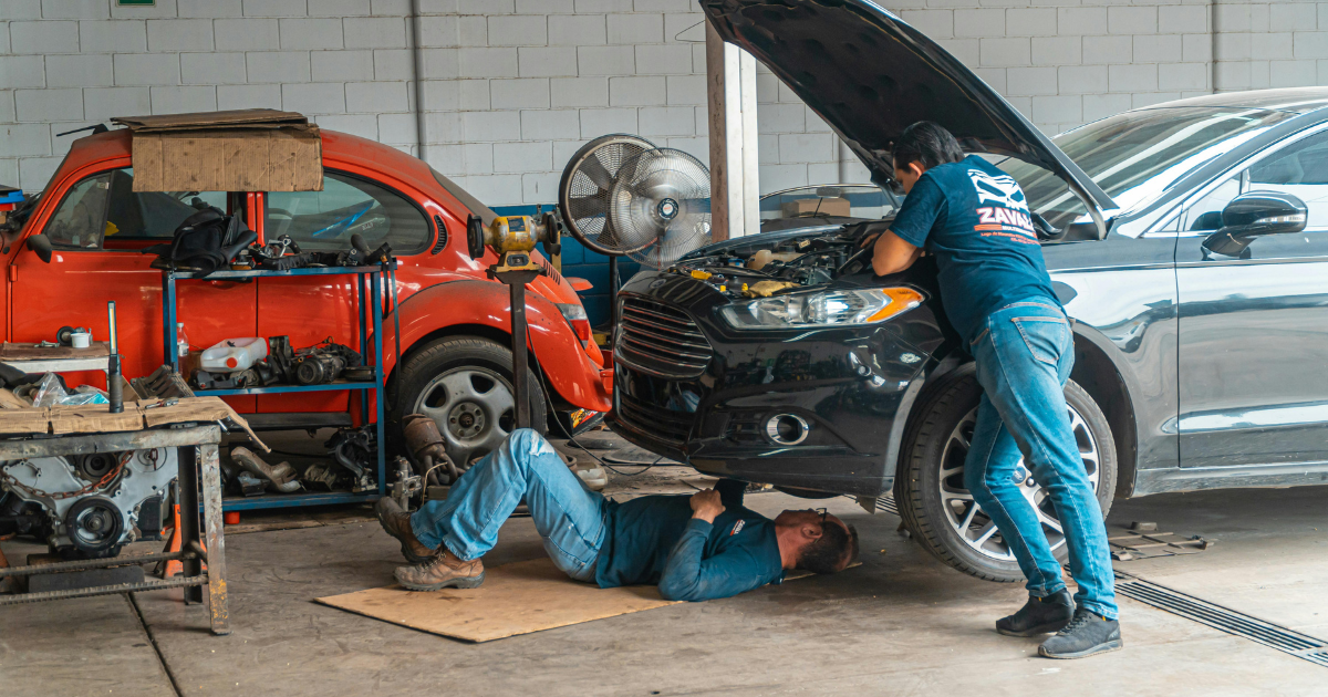 Two mechanics working on a vehicle during a routine car service in an auto repair workshop.