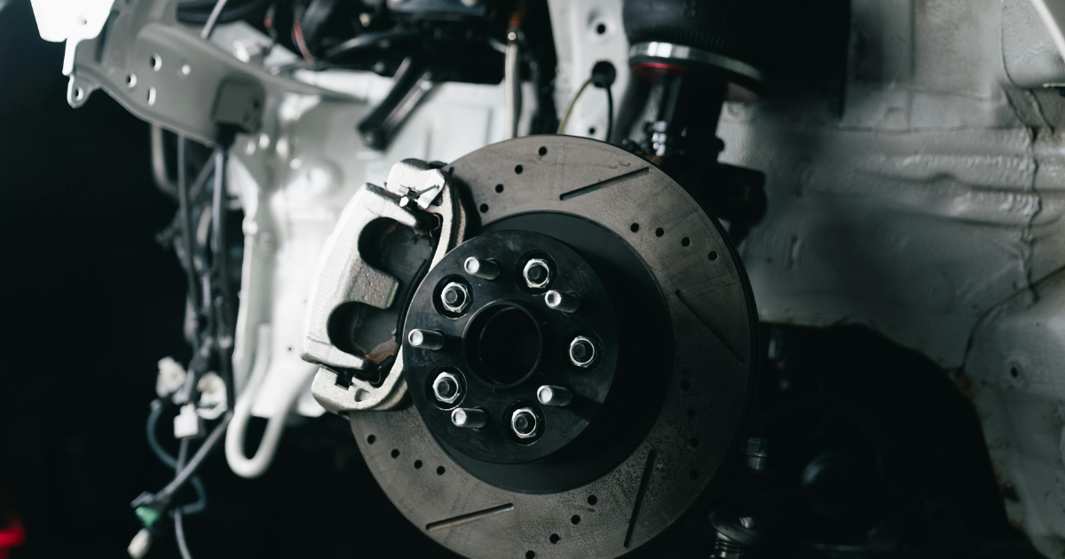 Close up of a car's brake disc and caliper, exposed with the wheel removed, showing rotor detail.