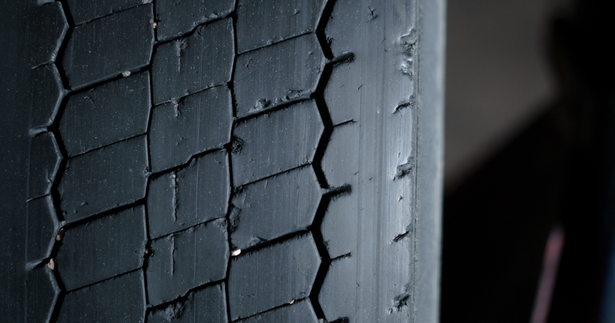 Close up of a car tyre showing worn tread pattern and cracking along the rubber surface.