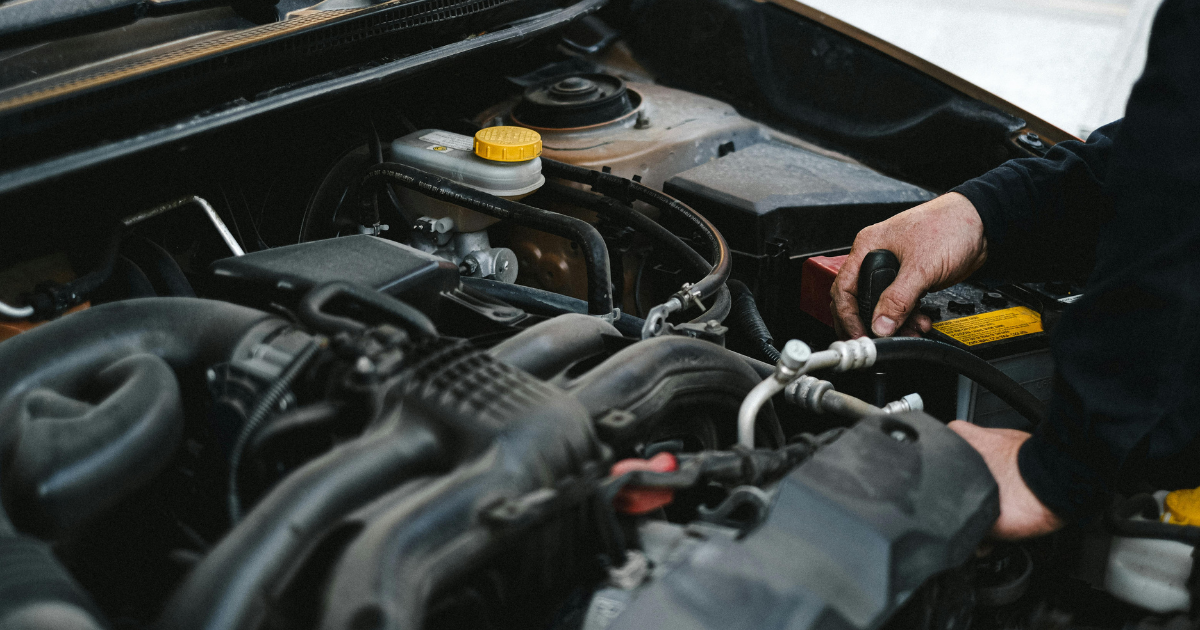 Mechanic inspecting a car engine bay, checking fluids and battery before a summer road trip.