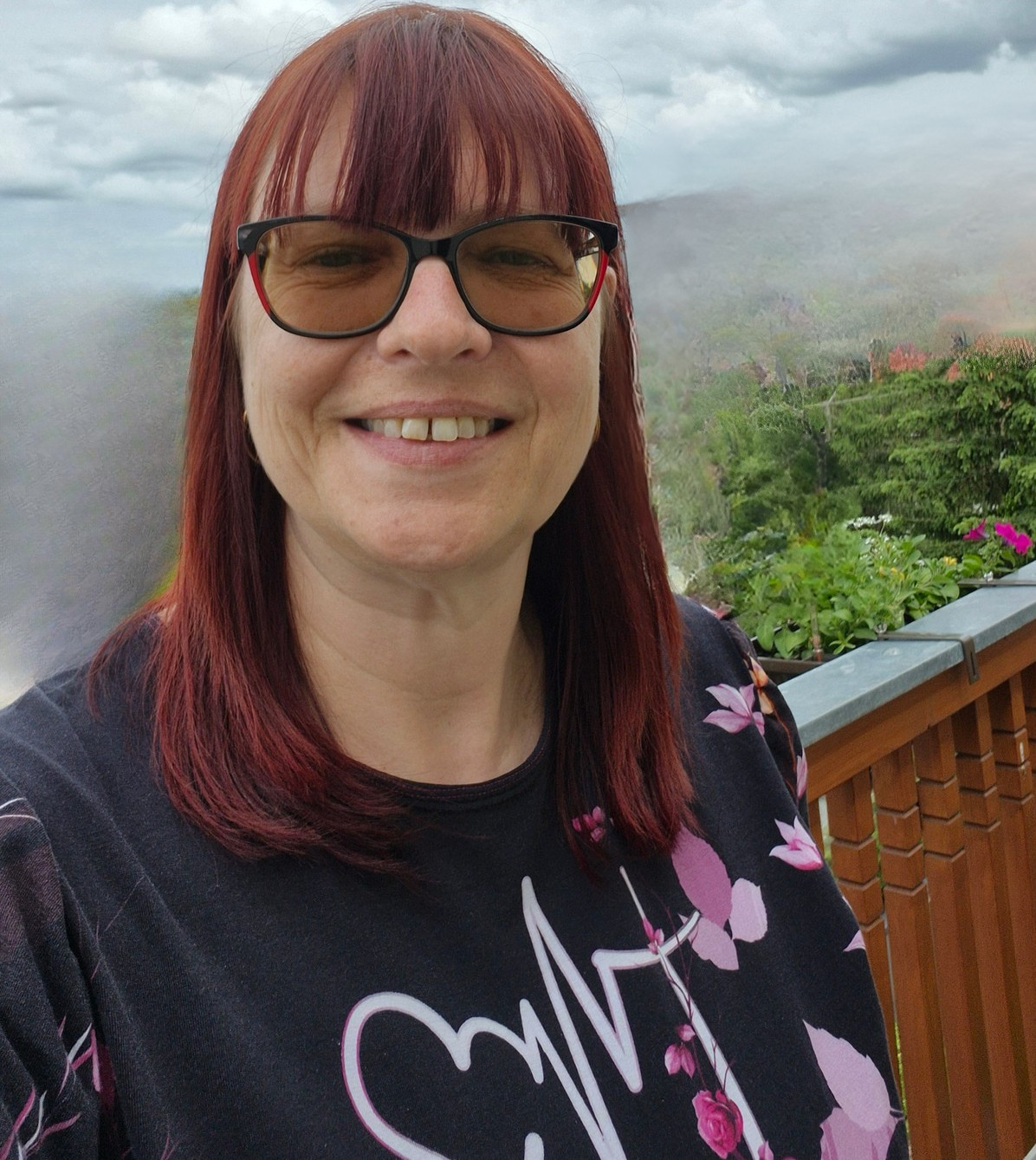 Marion Schumann, Mentorin für Frauen mit Lipödem, lächelt offen auf ihrem Balkon vor grünem Hintergrund
