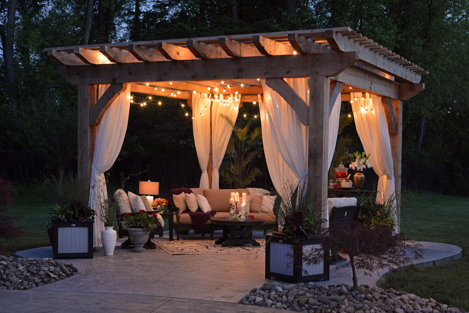 Illuminated timber pergola with curtains and outdoor seating at night