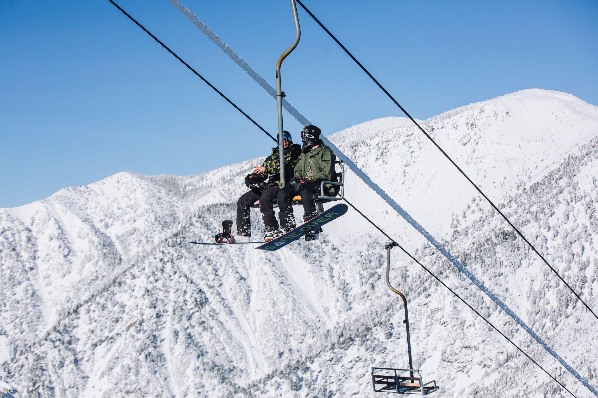 Riders on a Mt Baldy chairlift passing rime-frosted pines under a deep blue sky