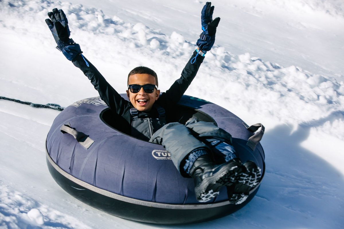 A dad on a snow tube with his arms in the air