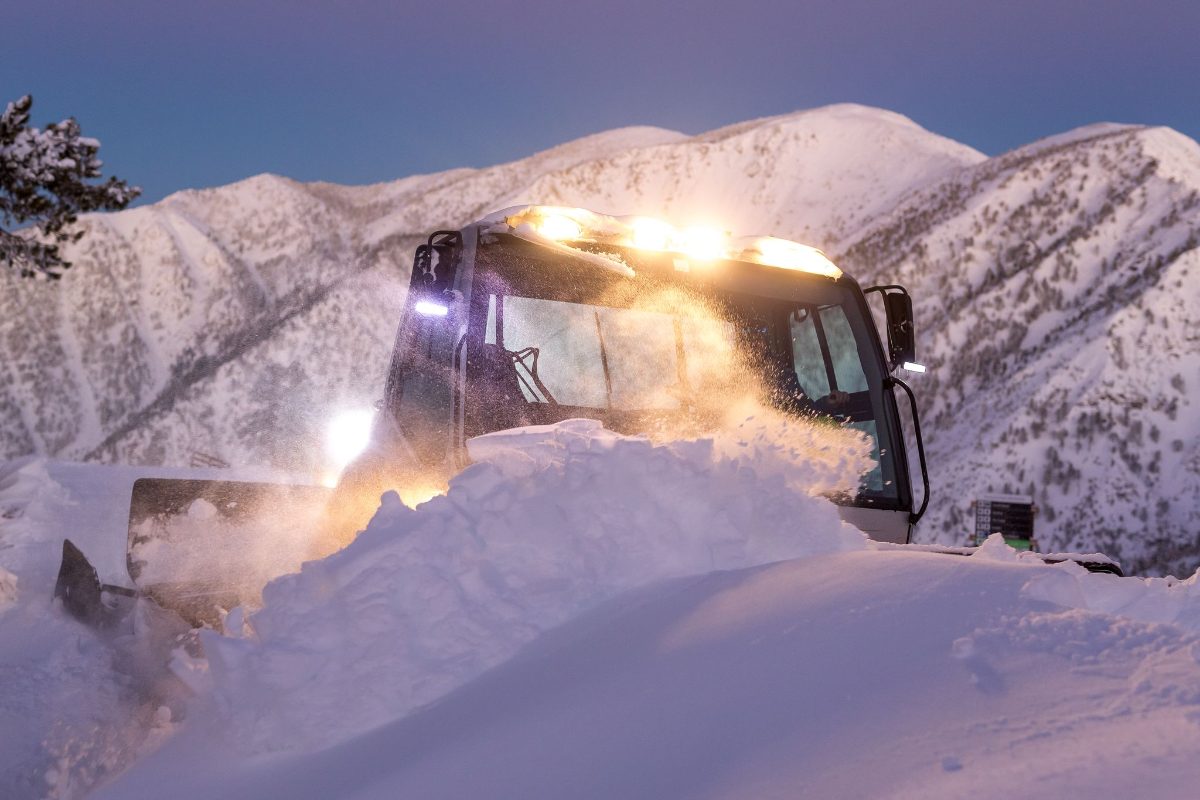 A snowcat grooming at night with its lights on