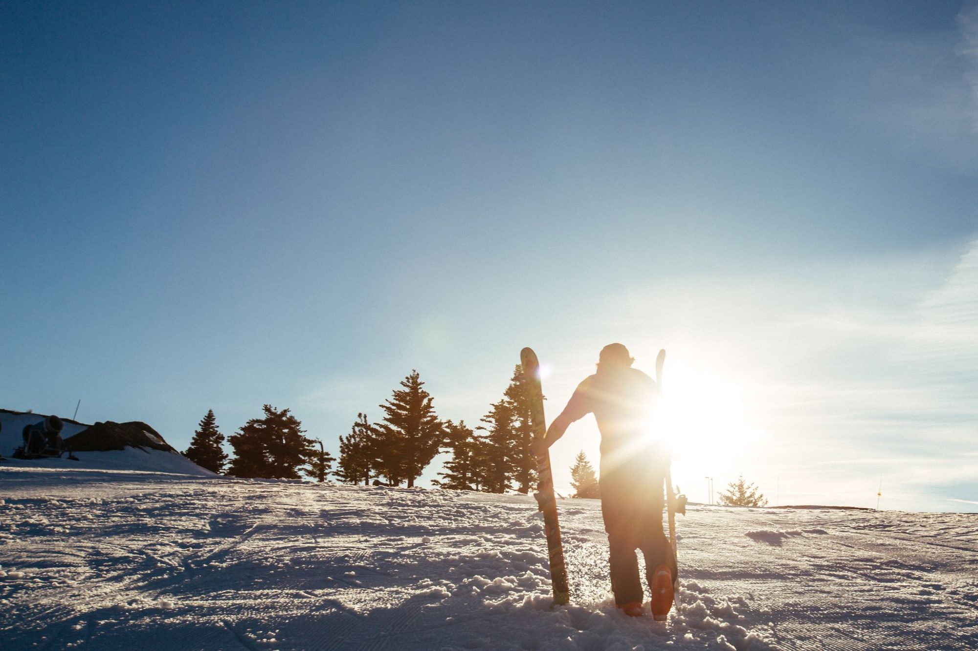 Skiers on the slope with the sun bursting over the ridge