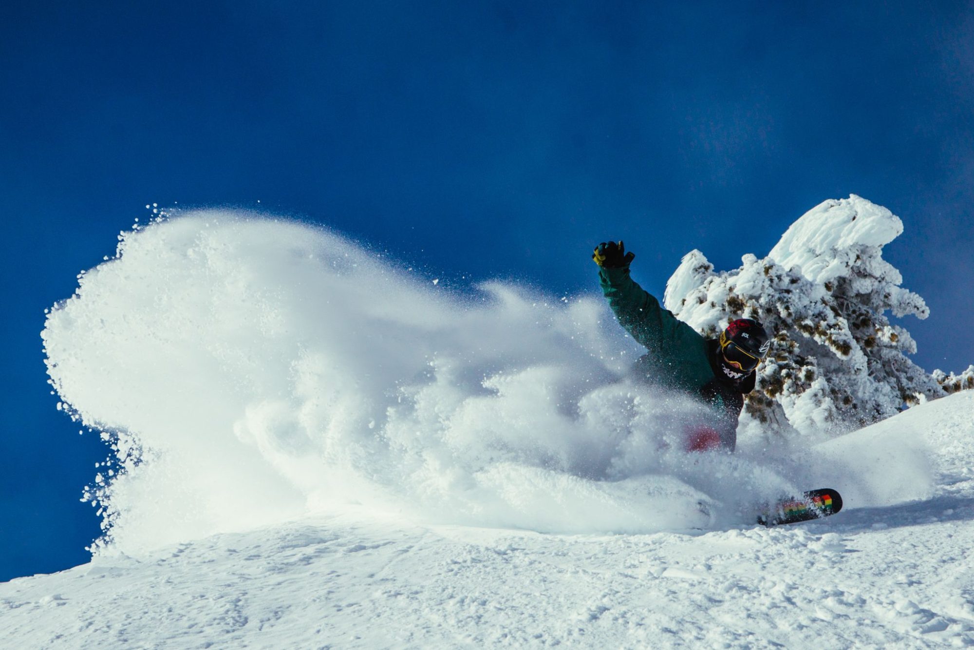 A snowboarder spraying powder under a blue sky