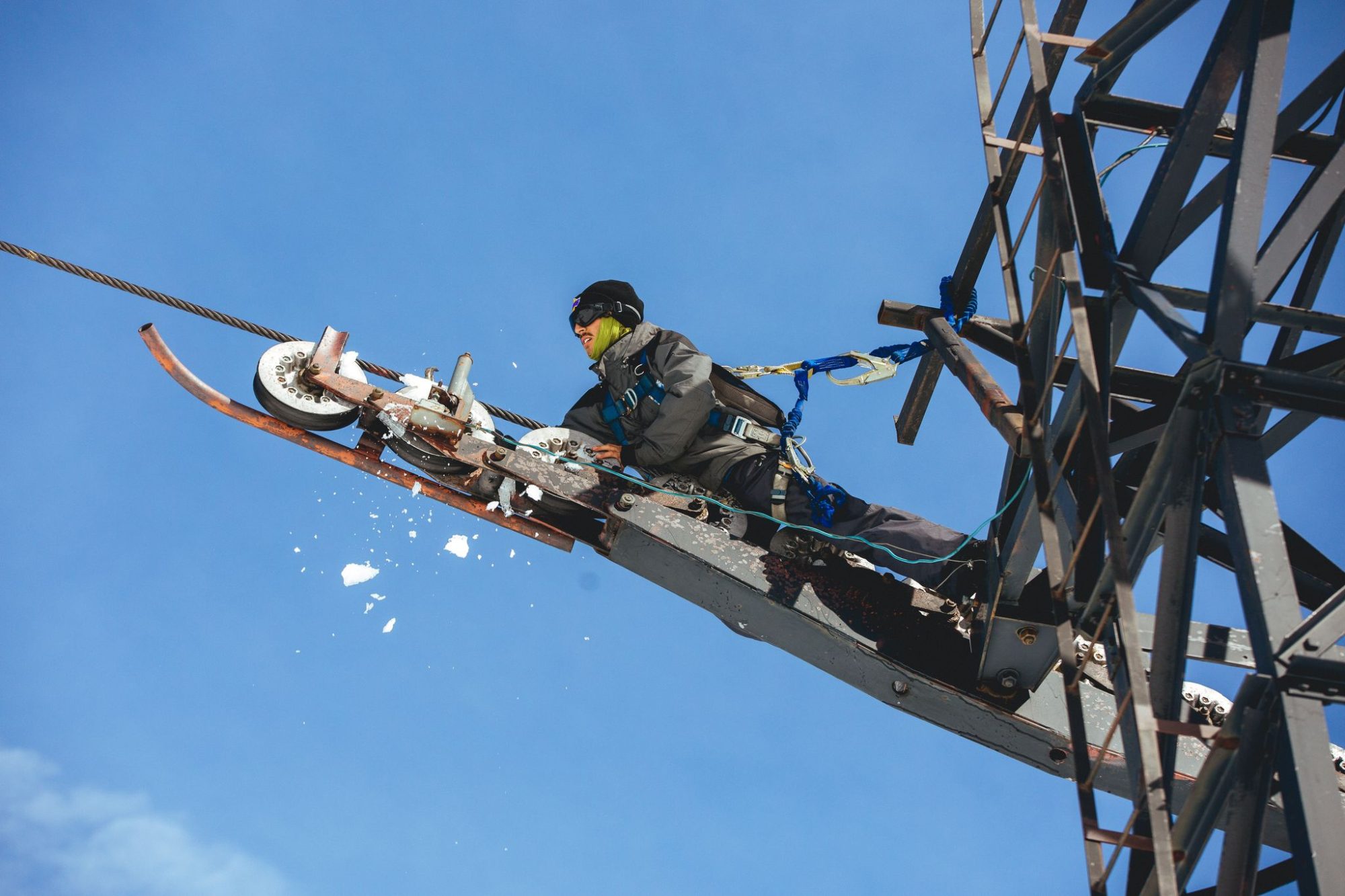 A lift mechanic working out on a tower crossarm against a blue sky