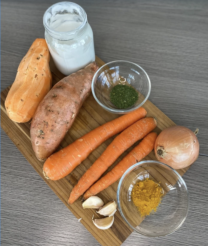ingredients for soup, sweet potatos, onions, carrots all on a cutting board