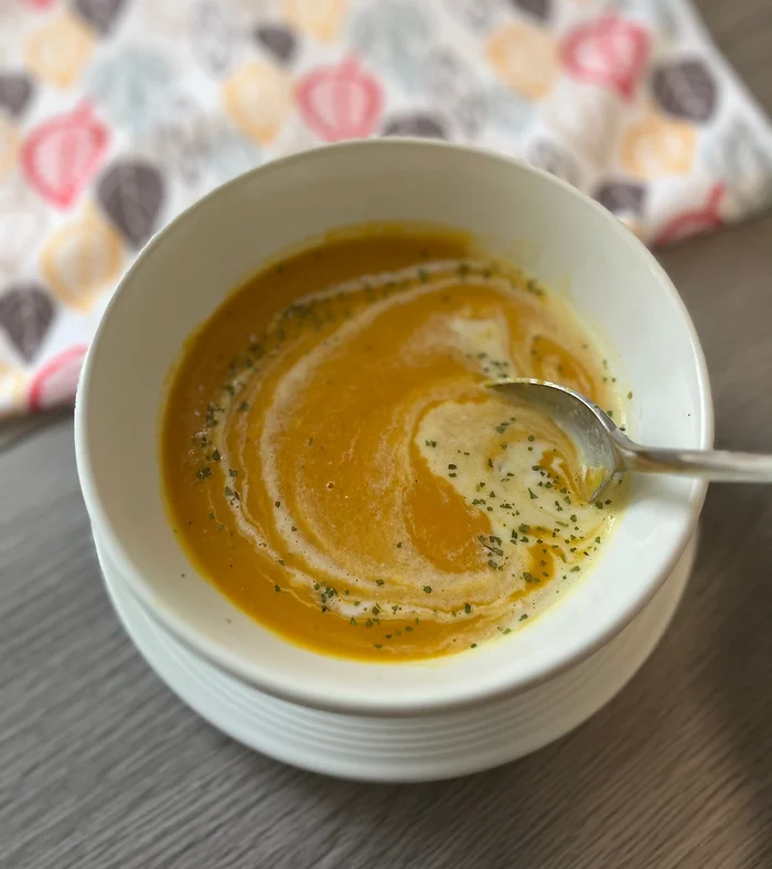 A bowl of golden sweet potato coconut curry soup served with a swirl of coconut milk and fresh herbs on a warm linen surface, representing cozy nourishing meals for busy women