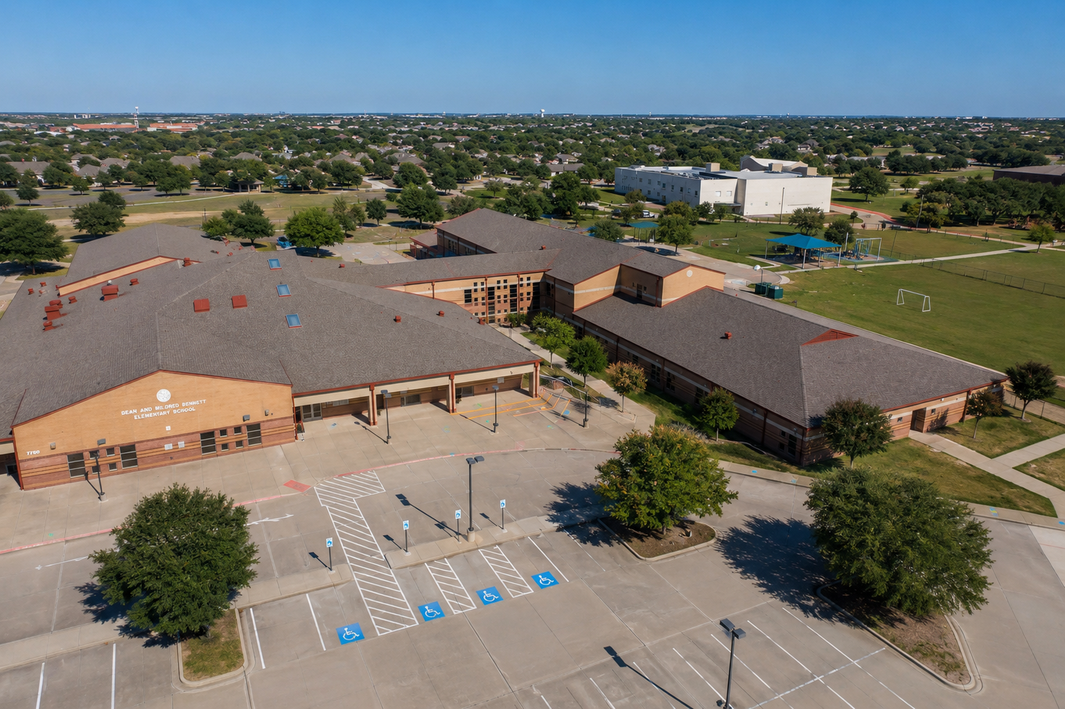 Aerial view of Dean and Mildred Bennett Elementary School in McKinney, Texas, showing the McKinney ISD school campus, playground, athletic fields, parking area, and surrounding residential neighborhoods.