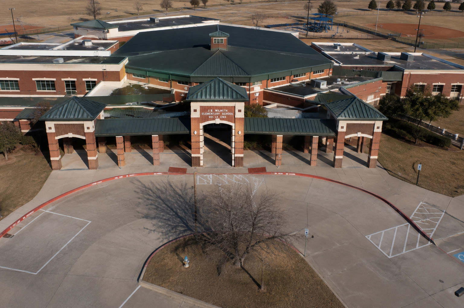 Aerial view of J.B. Wilmeth Elementary School in McKinney, Texas, showing the main entrance, McKinney ISD school campus, playground, and outdoor recreation areas.