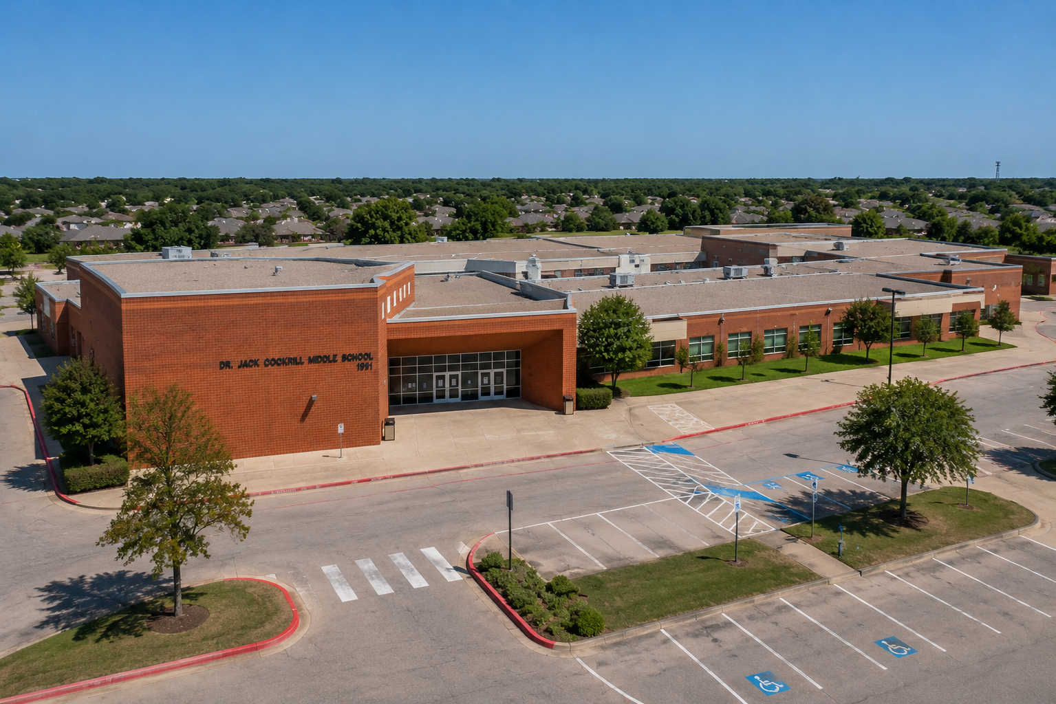 Aerial view of Dr. Jack Cockrill Middle School in McKinney, Texas, showing the McKinney ISD campus, main entrance, parking area, and surrounding residential neighborhoods.