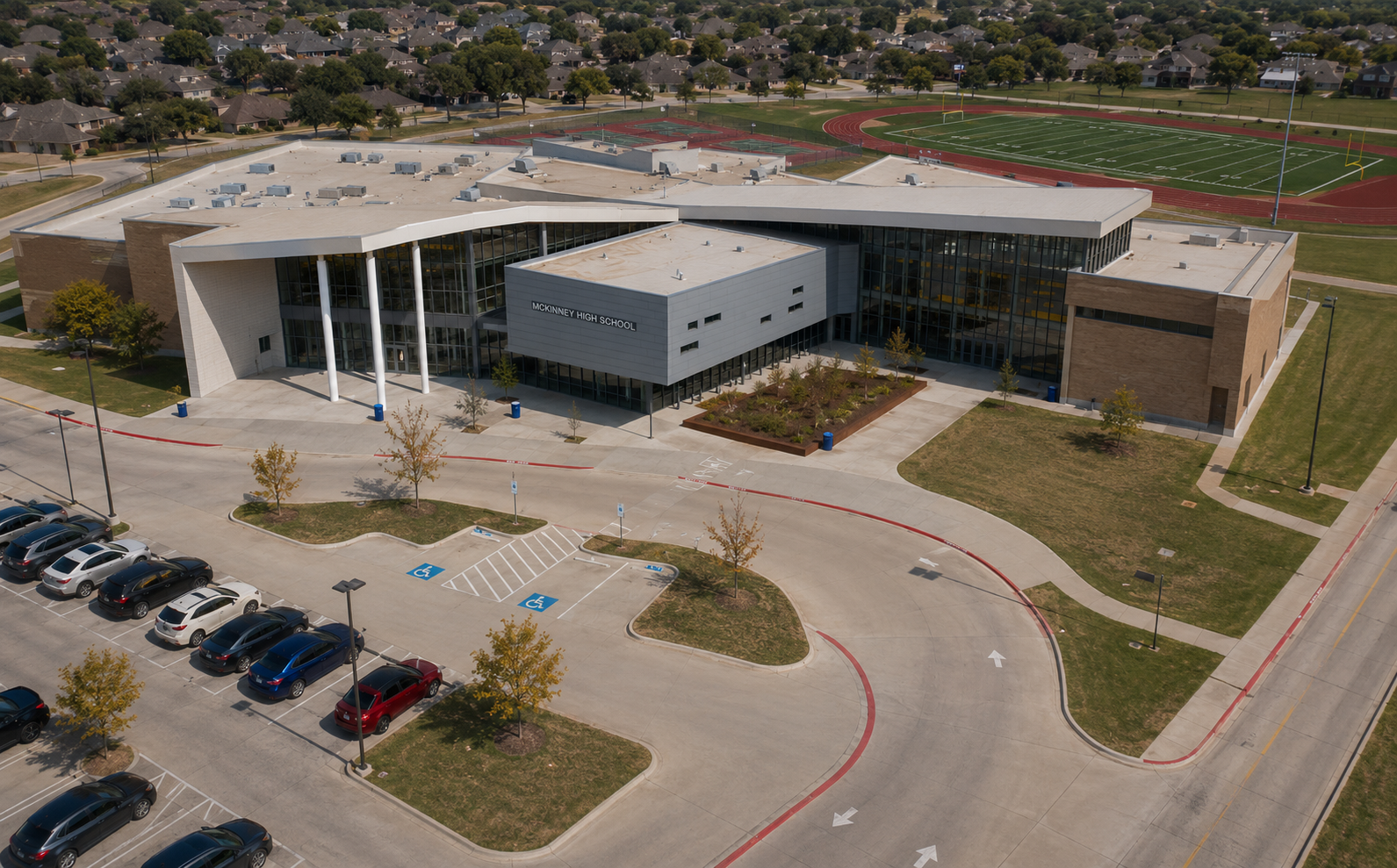 McKinney High School aerial view in McKinney, Texas, showing the school campus, athletic fields, football stadium, tennis courts, parking areas, and surrounding McKinney neighborhoods.