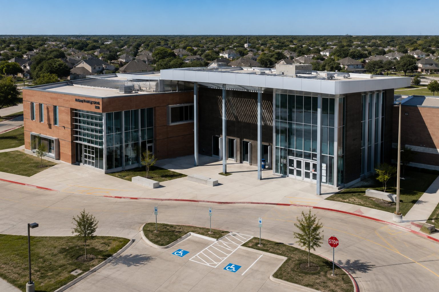 McKinney North High School aerial view in McKinney, Texas, showing the modern school entrance, brick and glass architecture, campus driveway, and surrounding residential neighborhoods.