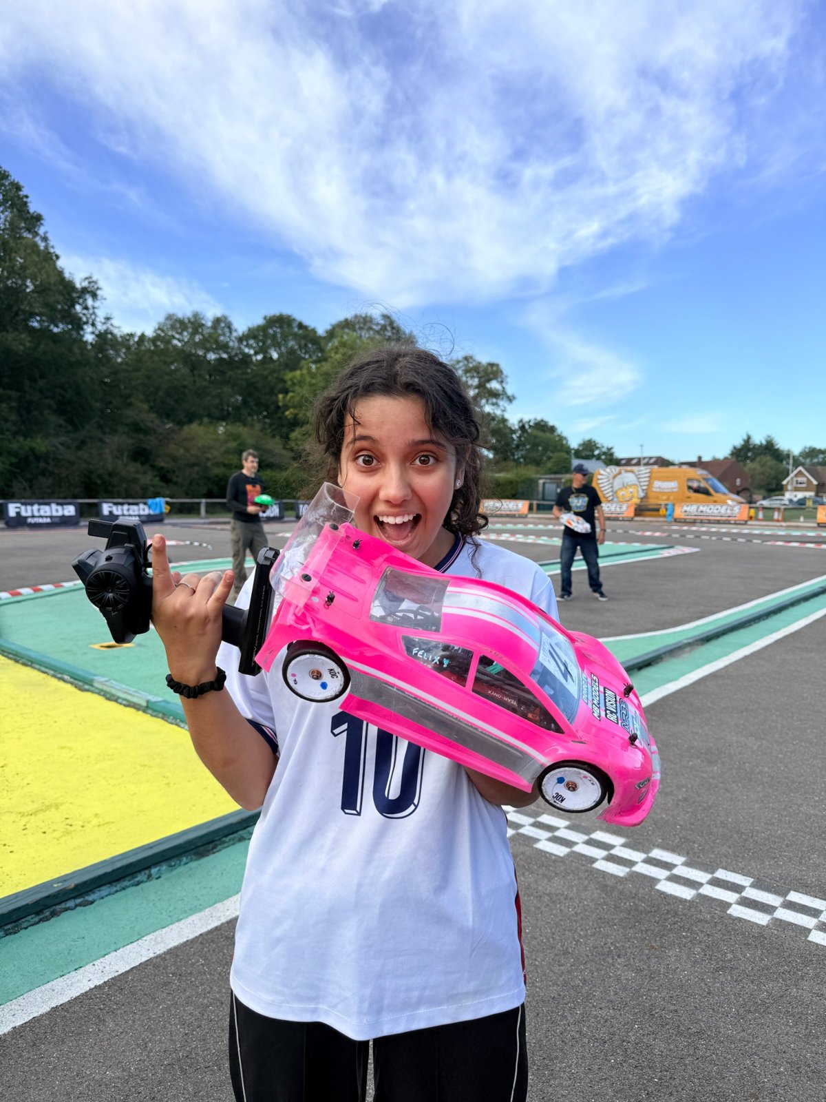 Aliza holding her pink race car and controller at the track, beaming