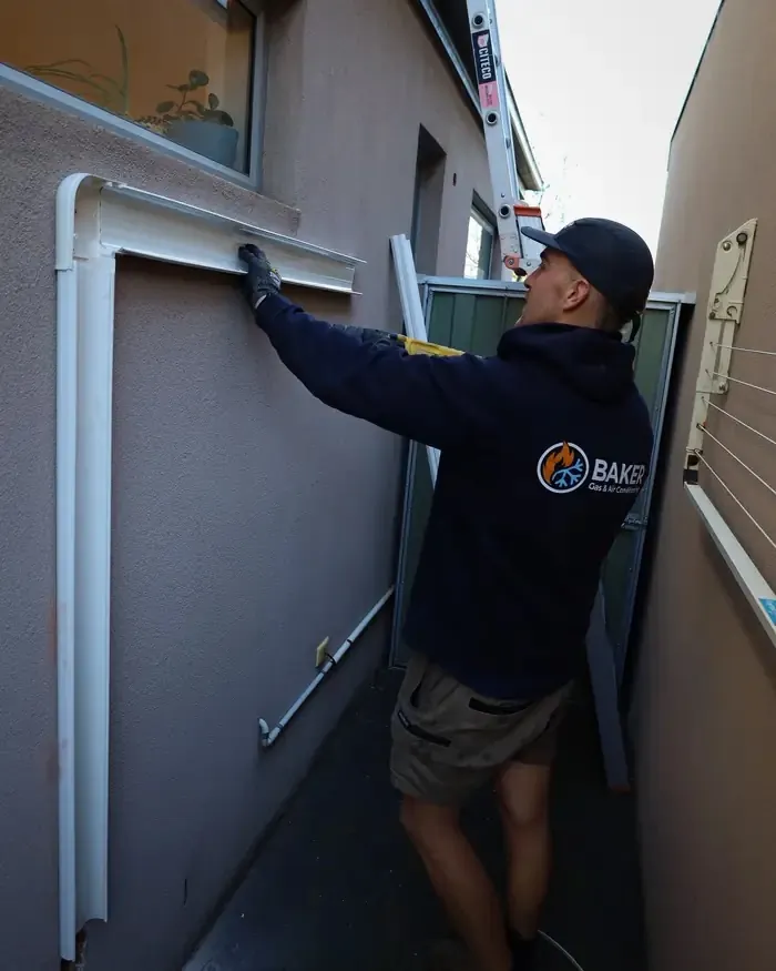 Baker technician working on an air conditioner installation in a narrow side passage