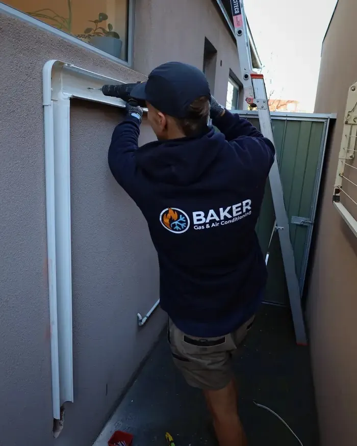Baker technician fitting pipework ducting to an exterior wall
