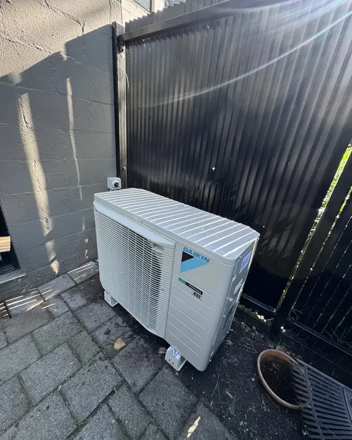 Daikin outdoor condenser unit installed on paving beside a fence