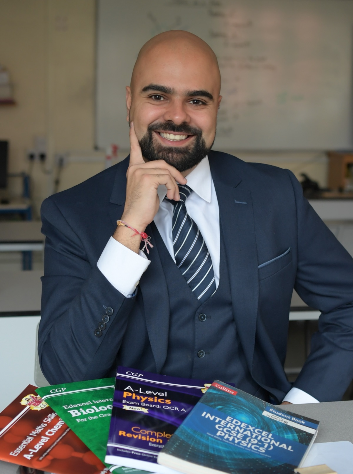 Mr. Pattni at a classroom desk with GCSE and A-level revision books