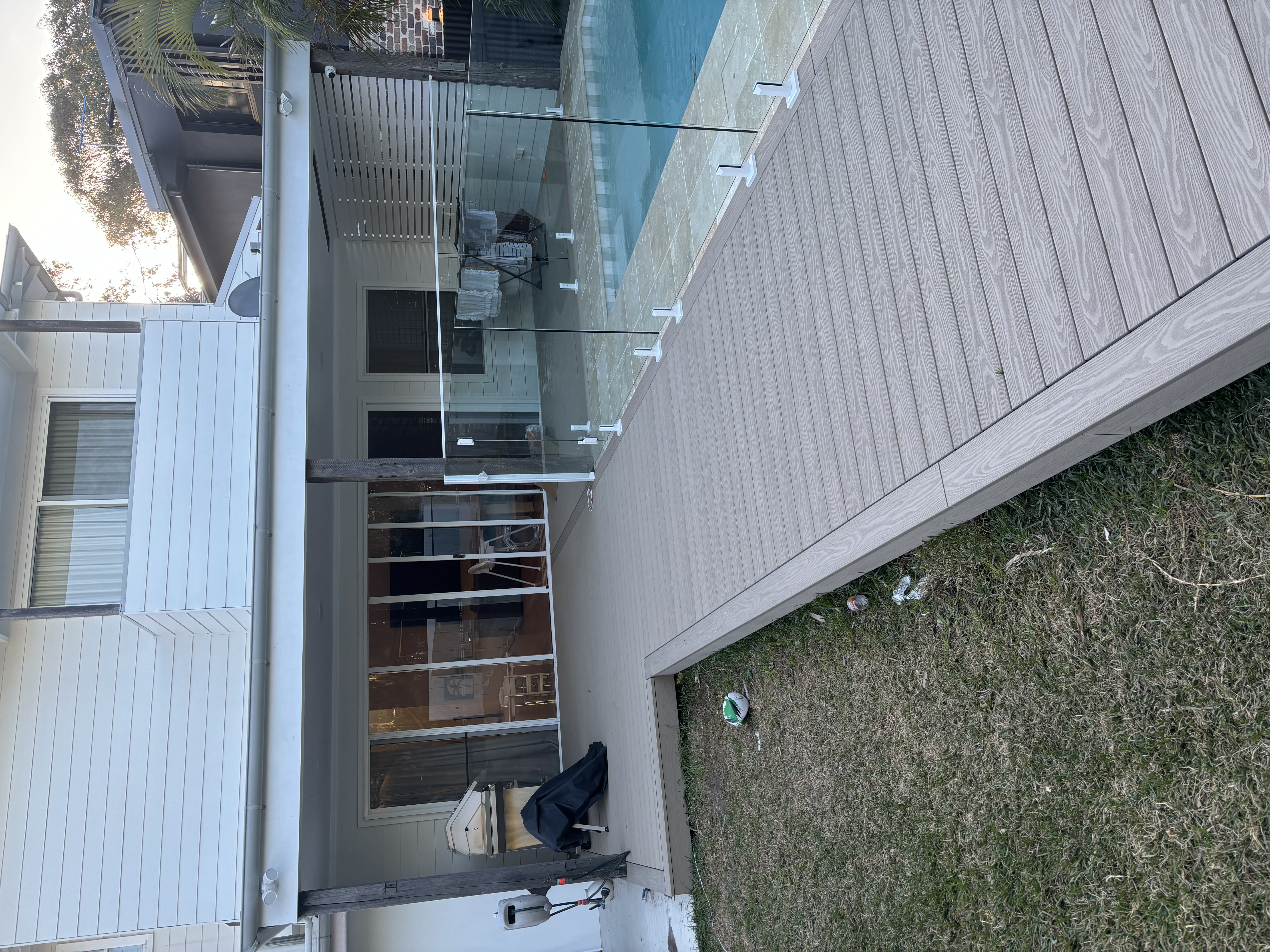 Composite deck boardwalk running beside a glass-fenced pool