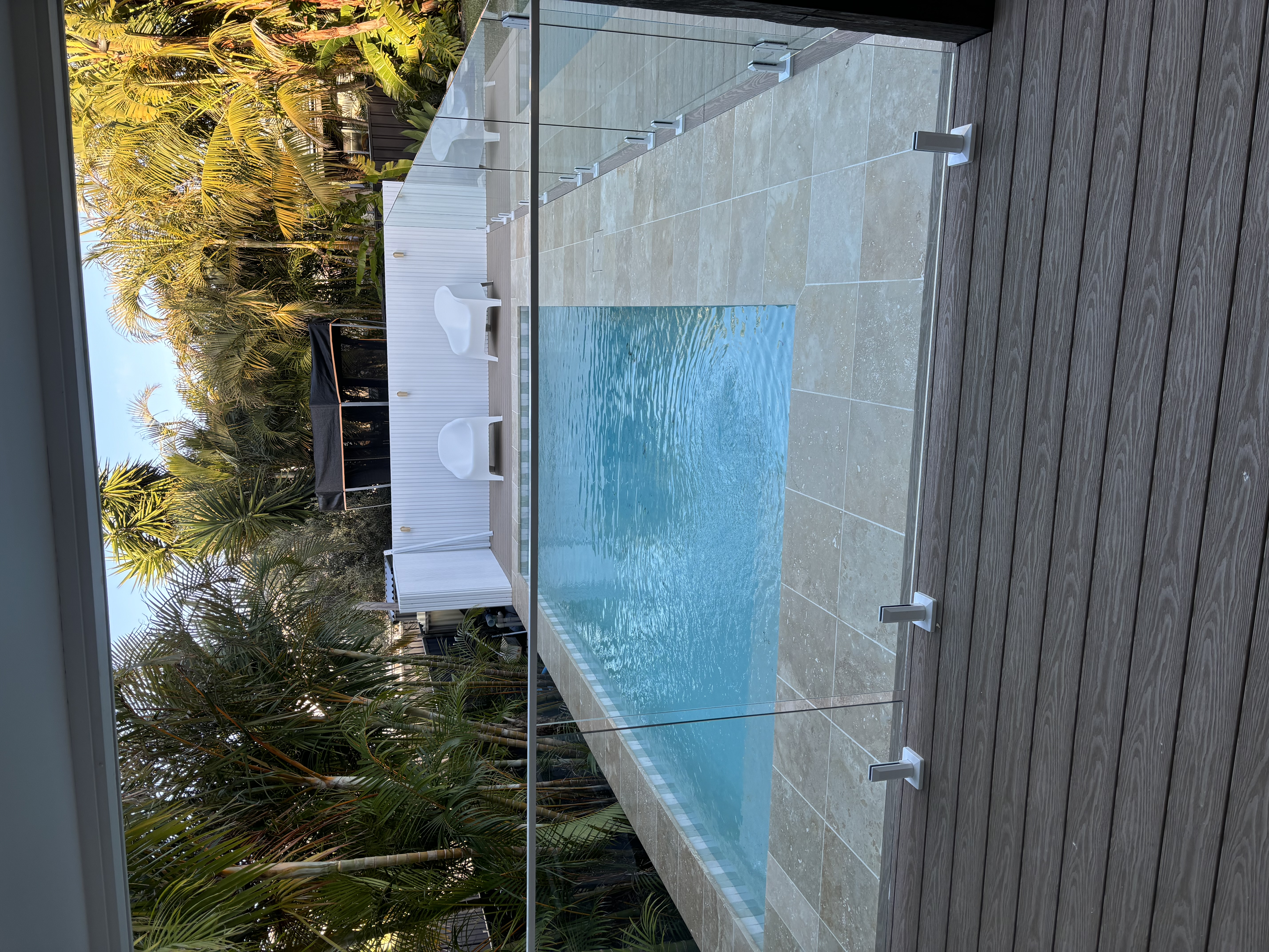 Composite deck meeting a sandstone pool surround with glass fencing