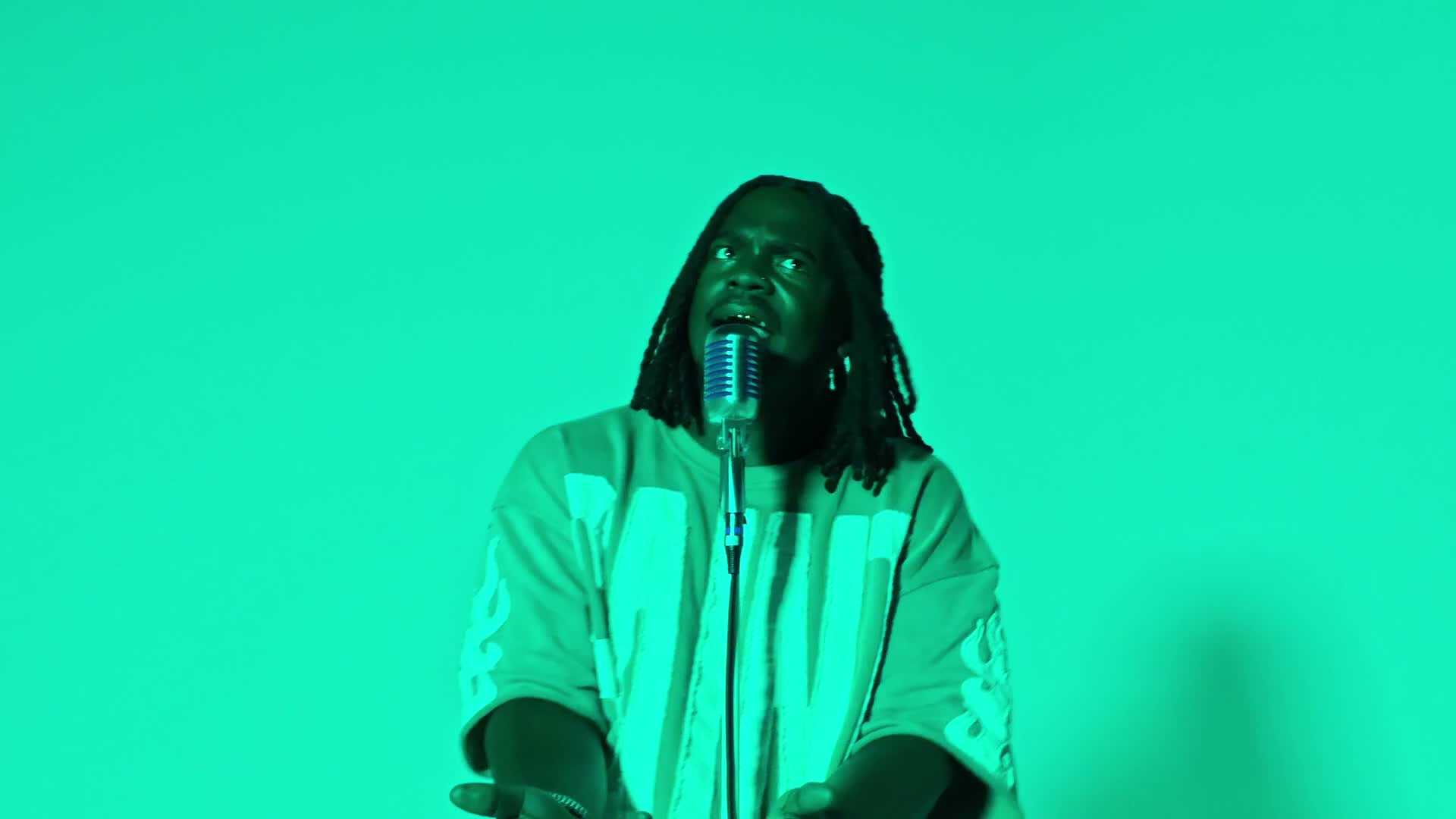 9thWardJay performing at a microphone under green studio lighting