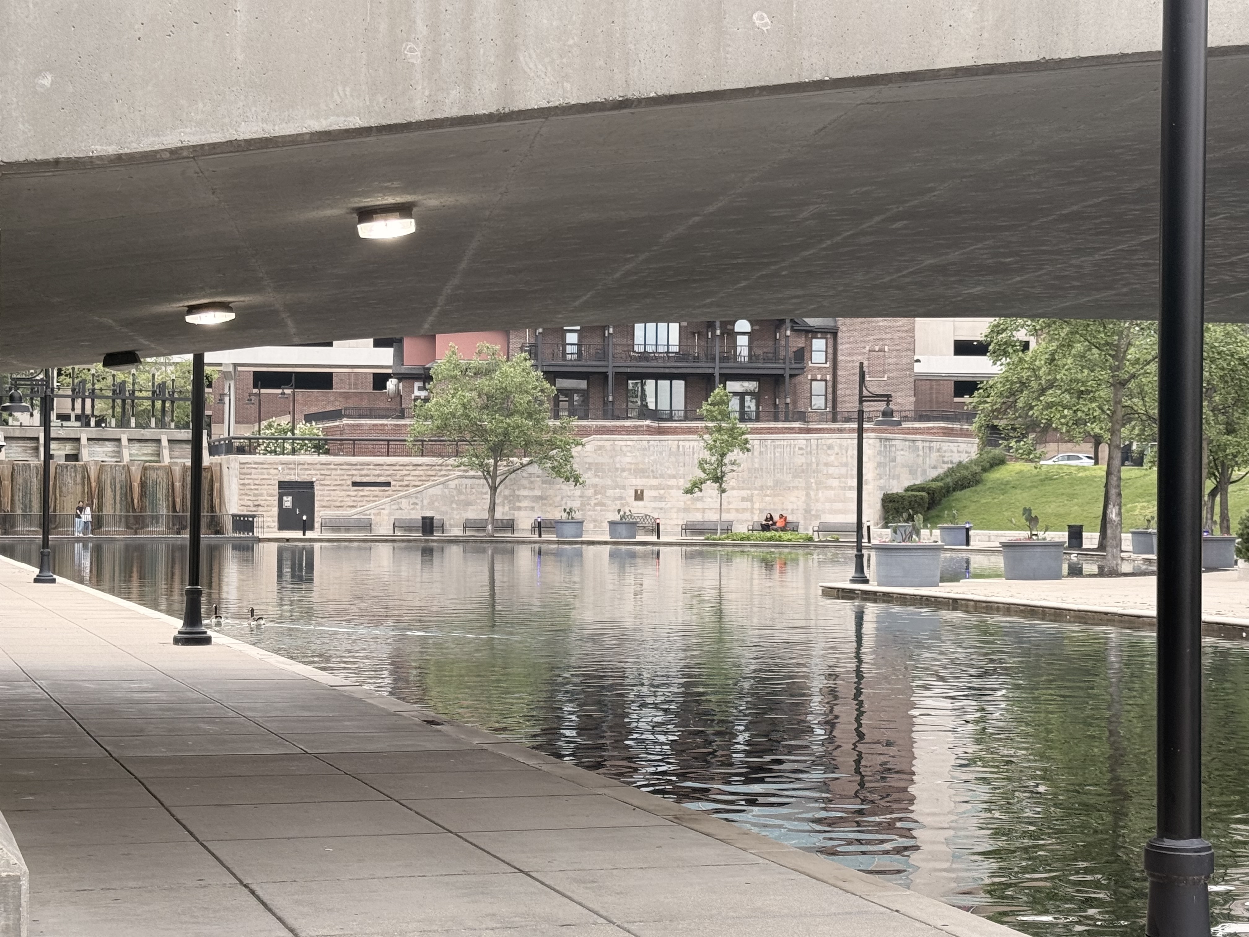 Downtown Indianapolis Canal view from the Cultural Trail with water, walking paths, trees, and city buildings.