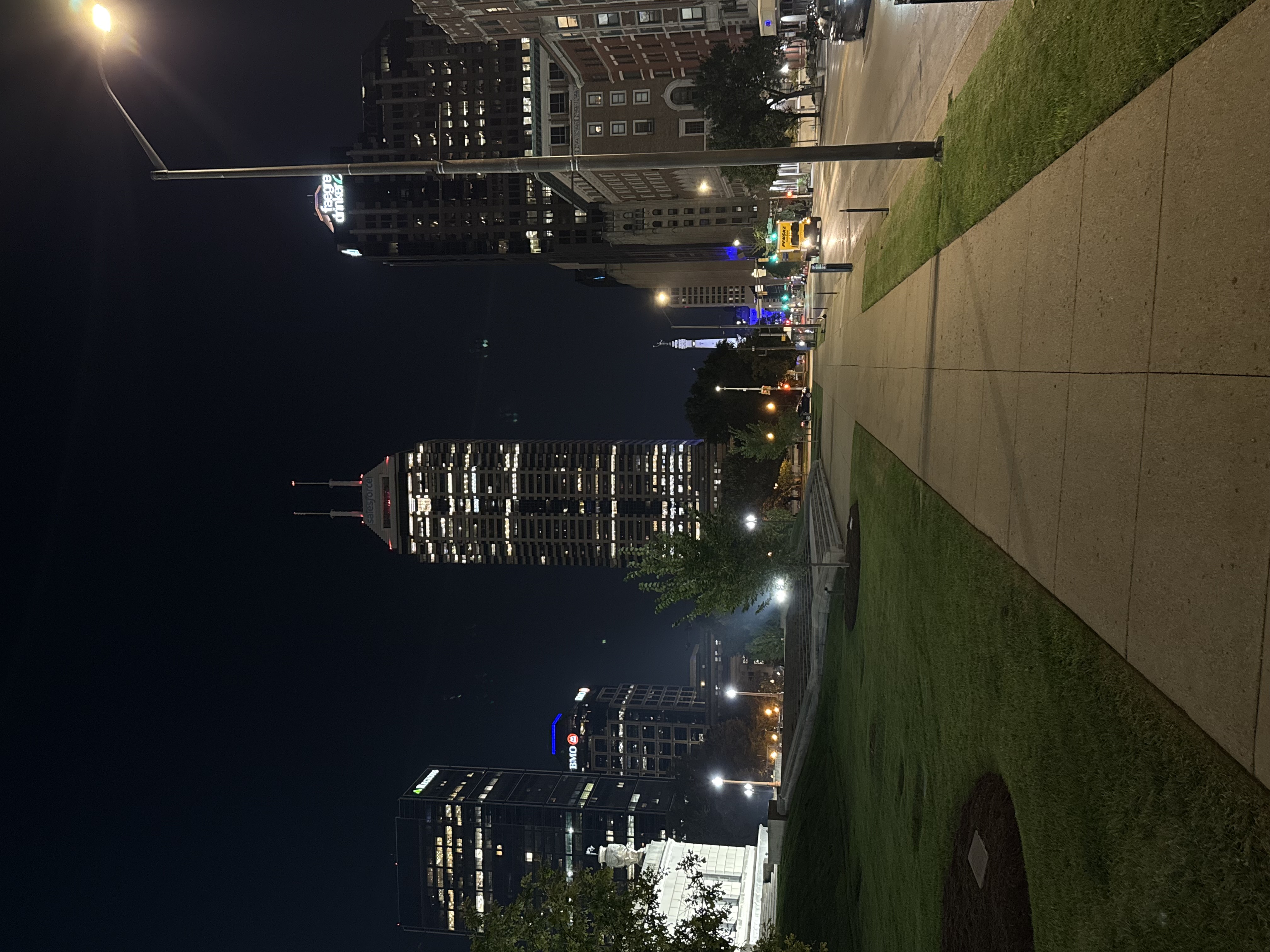 Downtown Indianapolis skyline at night with city lights, sidewalks, and Monument Circle in the distance.