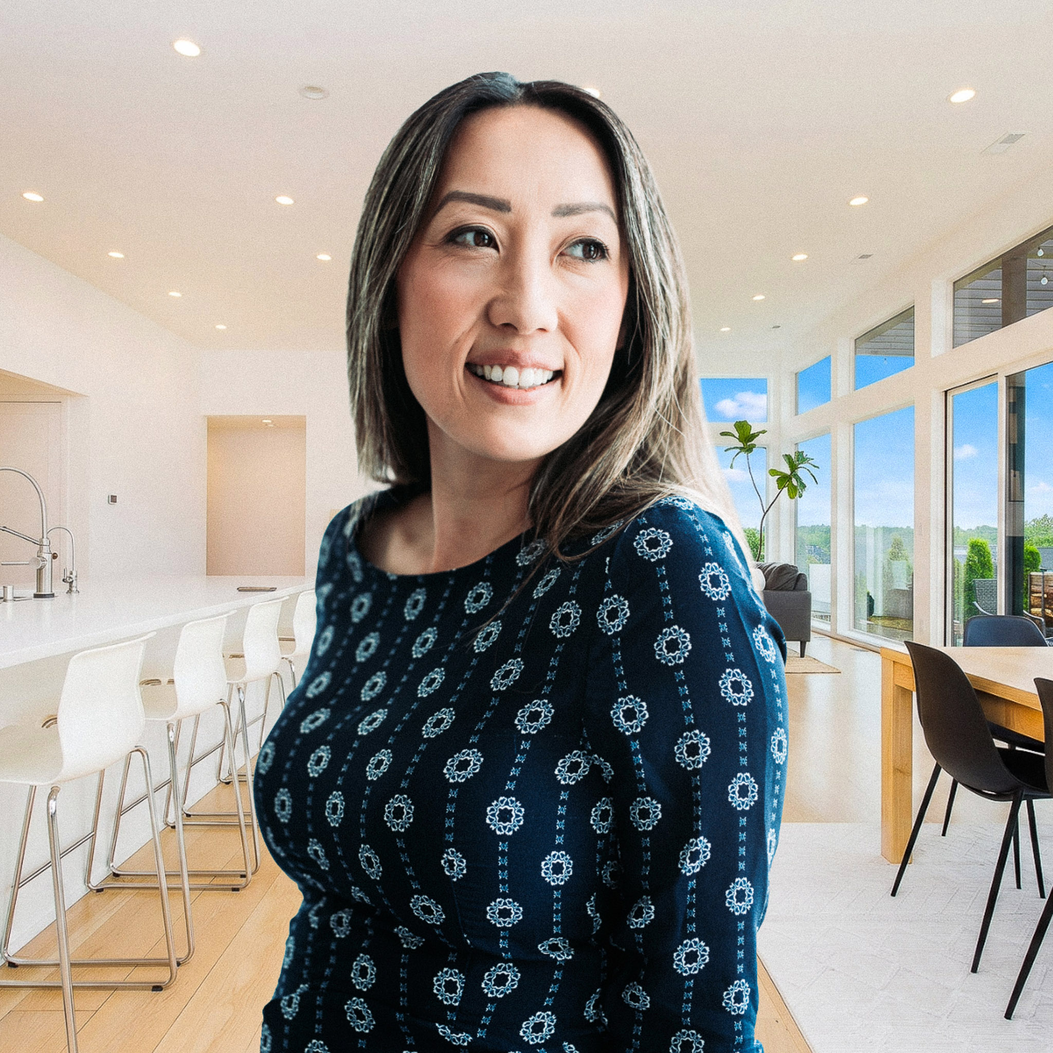 A woman, MyLee Corona Realtor, standing center frame with white suit and smile. Background of a luxury living room with fireplace, chairs and blue couches.