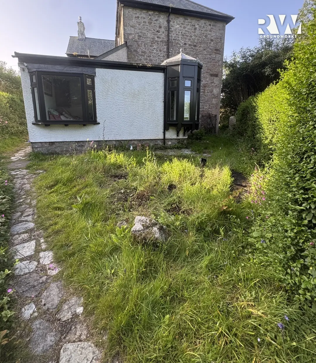 Wendron rear garden before: overgrown grass beside the hedge where the new patio now sits