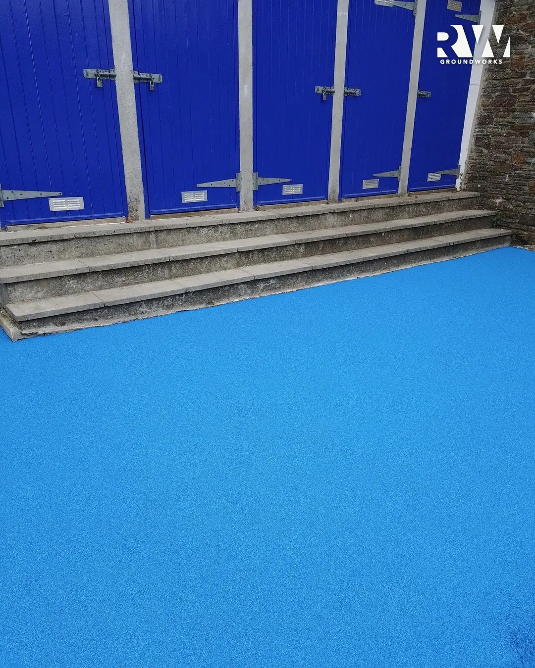 Blue wet-pour safety surface finished up to the steps and blue store doors at Flushing School