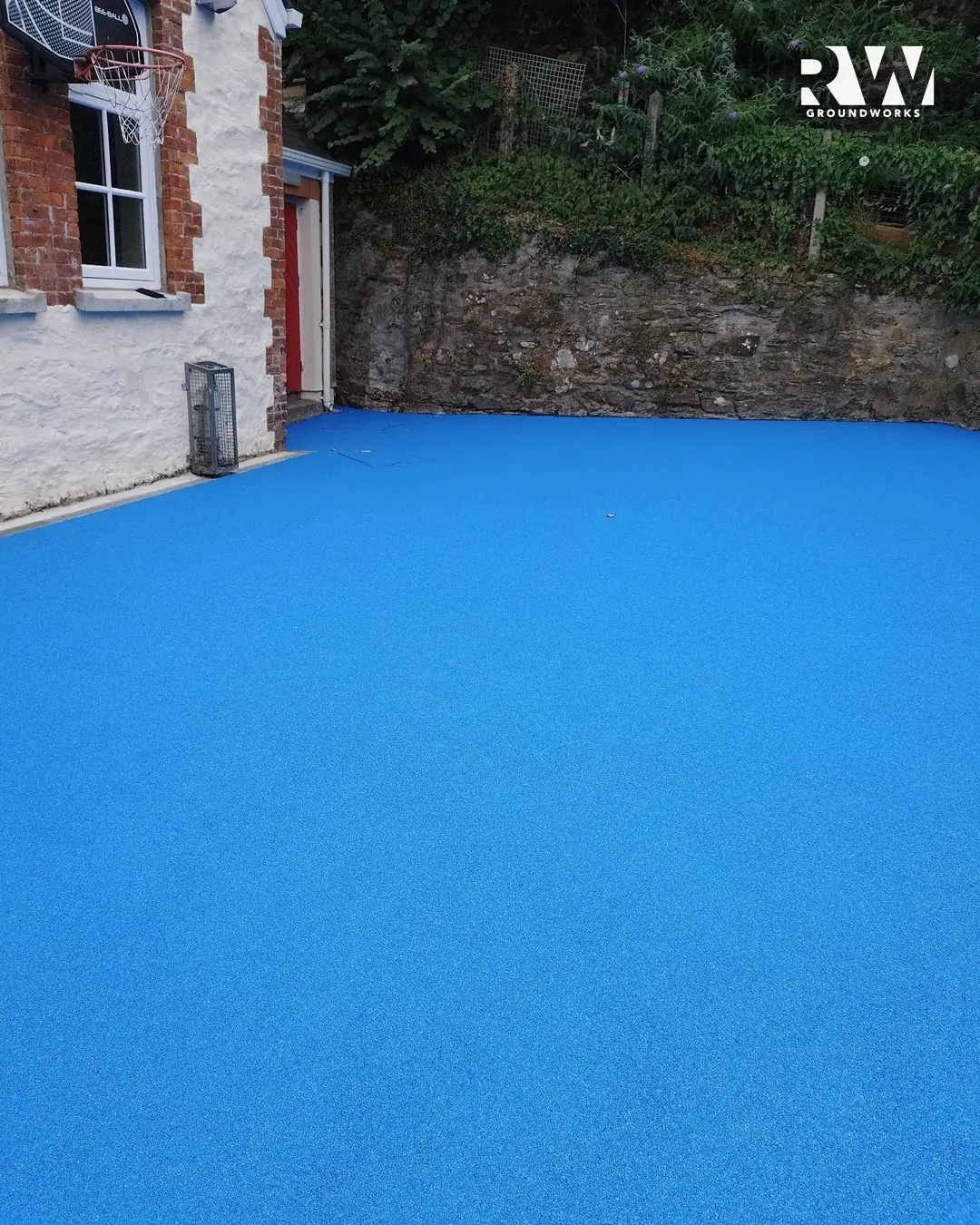 Finished blue wet-pour playground beside the school wall at Flushing School