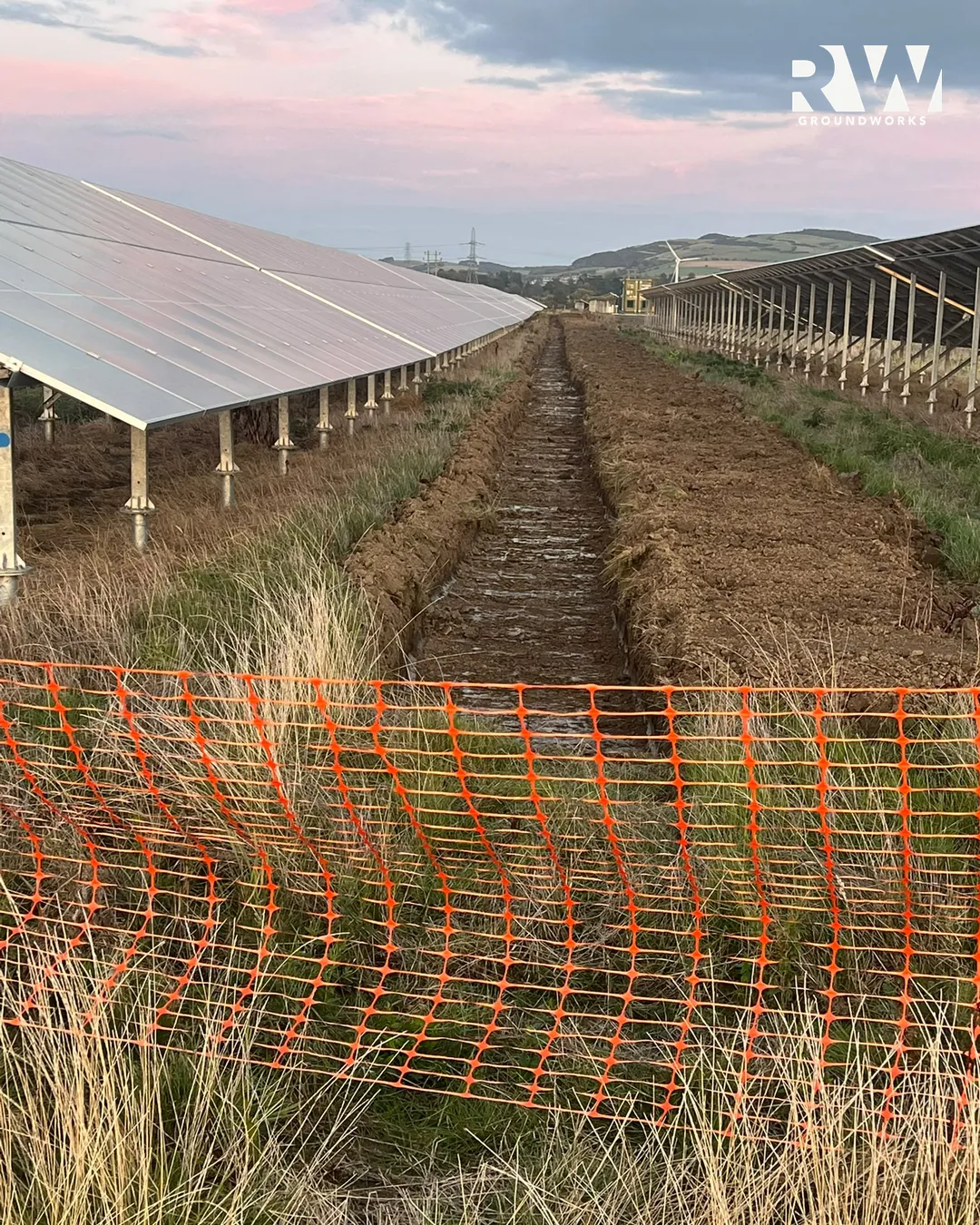 Drainage trench with orange safety fencing beside the solar panels