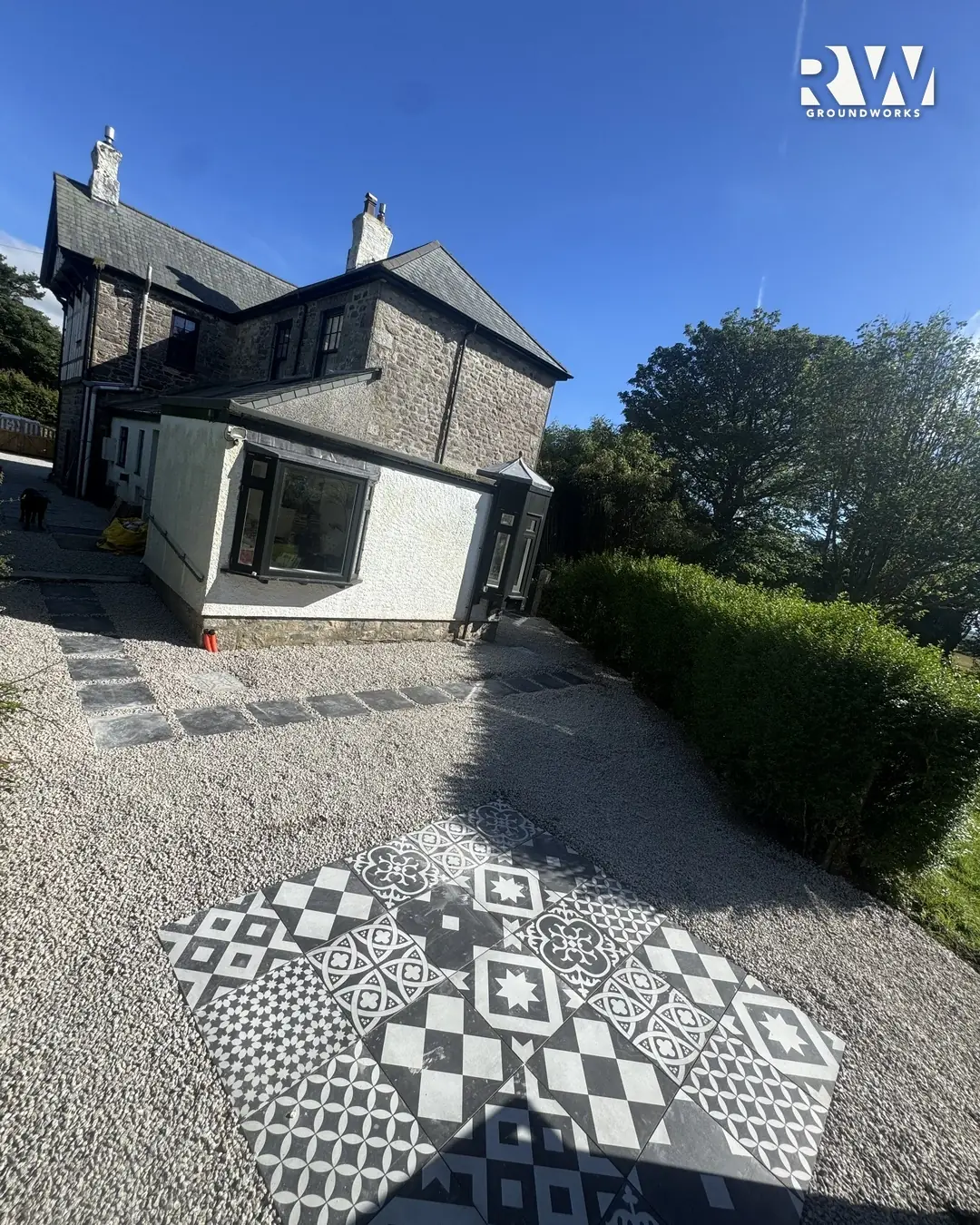 Patterned black and white tile patio set in gravel at the rear of the house in Wendron