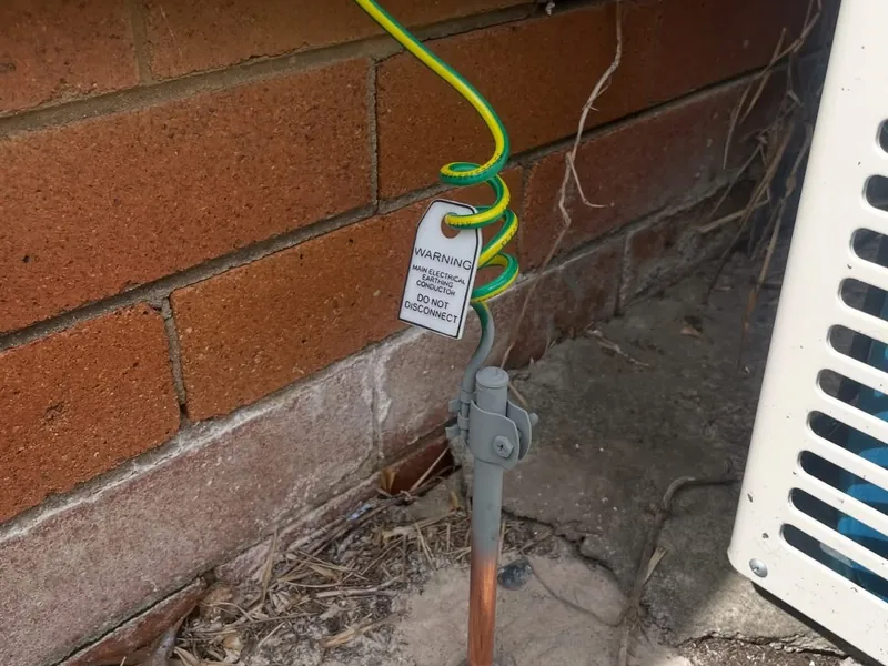 Main earth stake and earth cable with a warning tag beside a brick wall