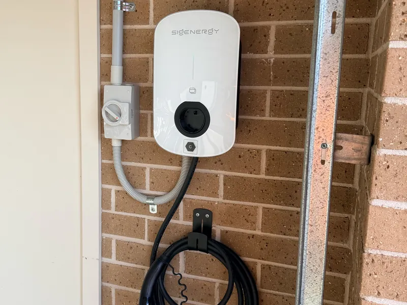 Sigenergy EV charger mounted on a brick wall next to an isolator switch