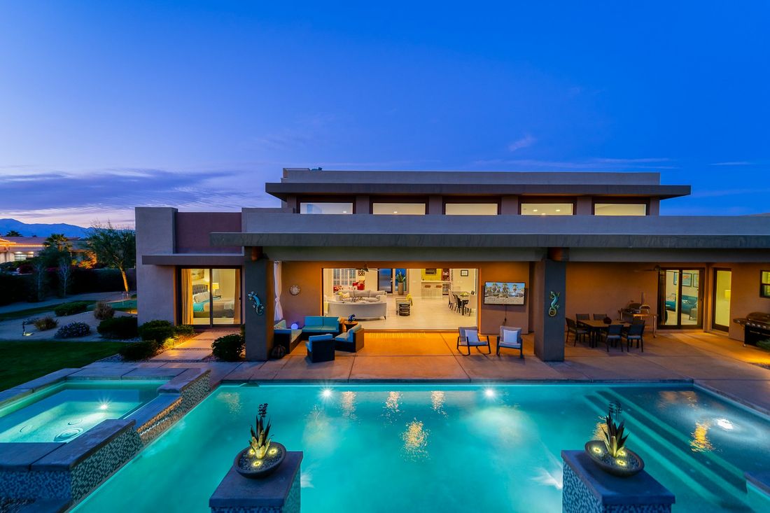 Modern home with a lit pool and outdoor lounge at twilight