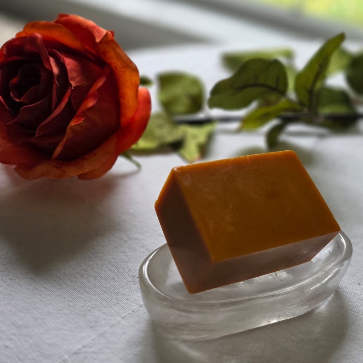 Golden Calm turmeric soap on a crystal dish beside an orange rose