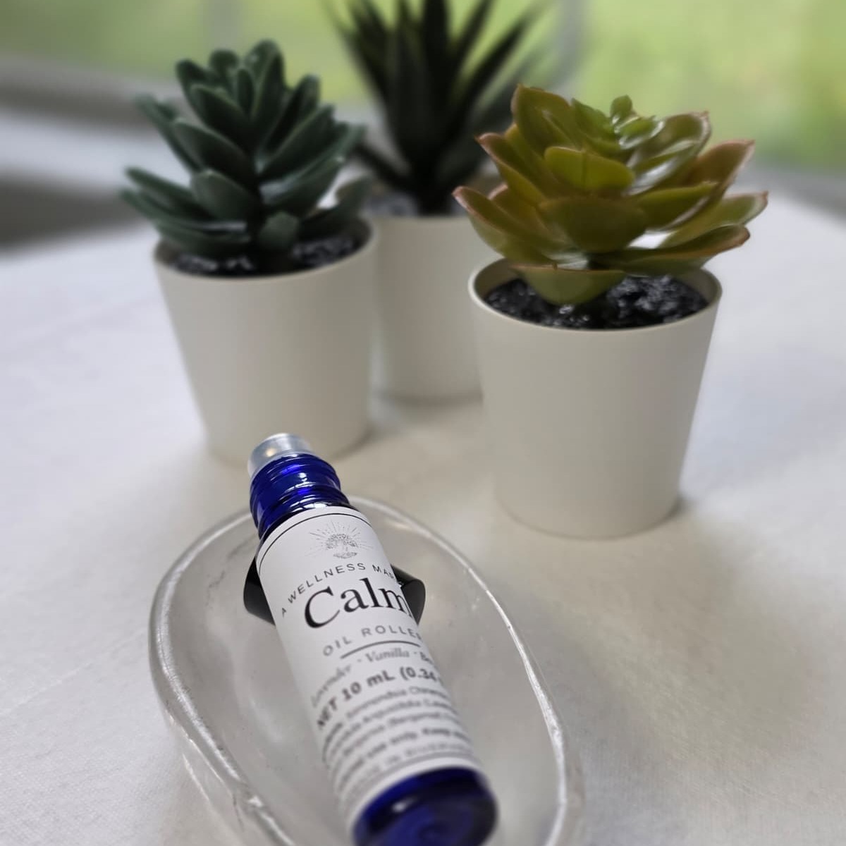 Calm oil roller in a blue glass bottle on a crystal dish with potted plants