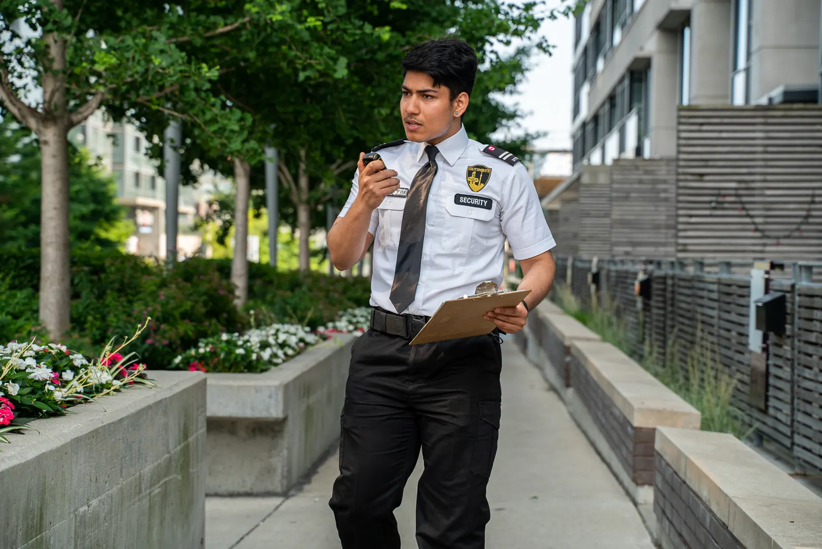 Uniformed security guard with a radio and clipboard posted at a building entrance