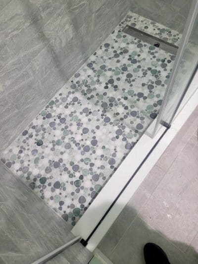 Unique pebble stone shower flooring with a linear drain