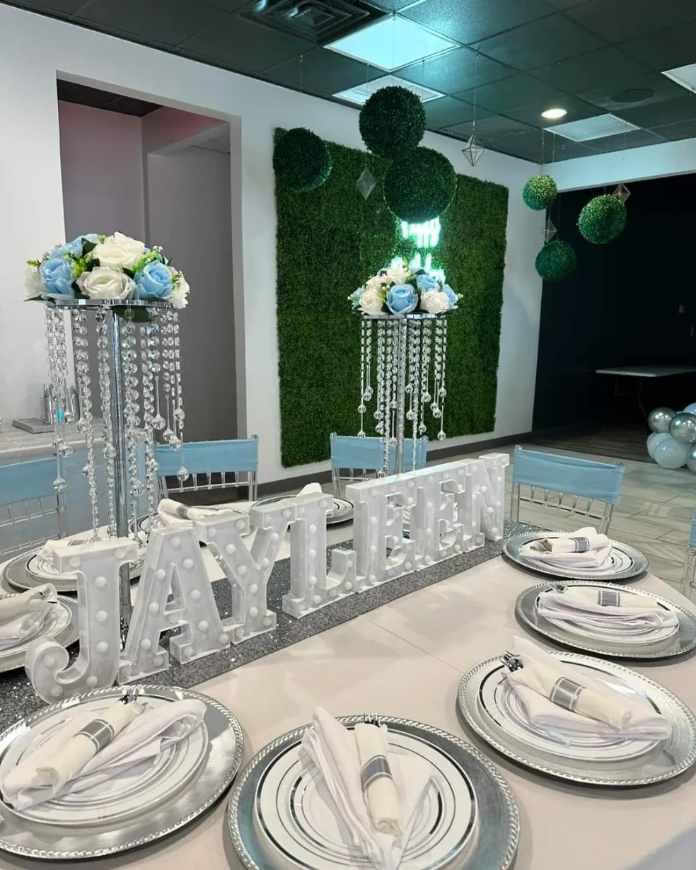 A greenery wall with white floral arrangements framing the head table