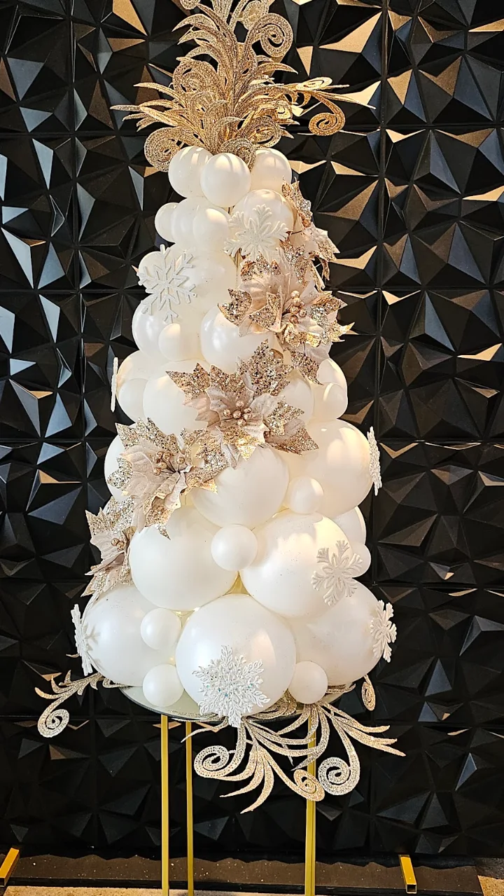 An ivory and white balloon tower trimmed with gold filigree, set against a black geometric wall
