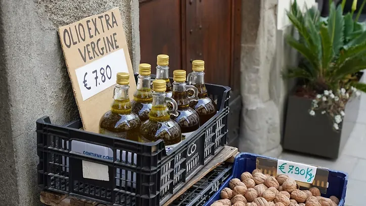 Bottles of extra virgin olive oil in a crate at a street stall, with a handwritten price sign