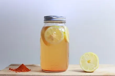 Glass jar of lemon water with lemon slices, beside half a lemon and a small pile of ground spice